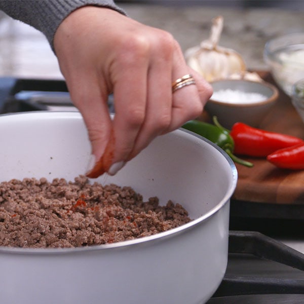 Sprinkling chili powder over ground beef